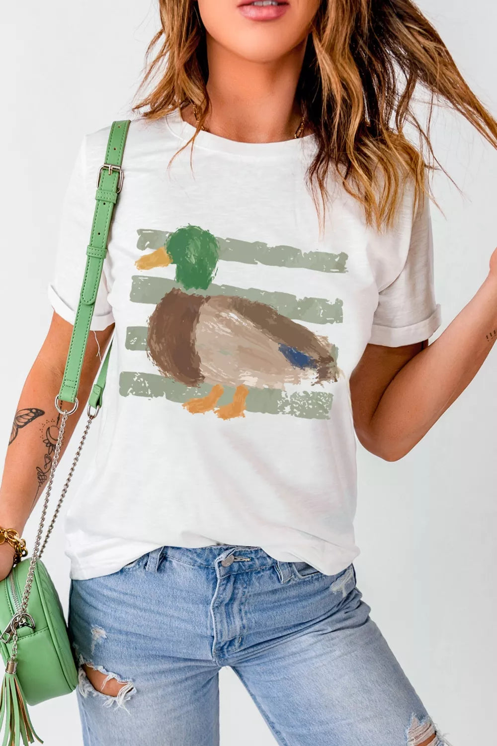 White short sleeve graphic tee with a painterly mallard duck design over muted green stripes, styled with camo shorts.