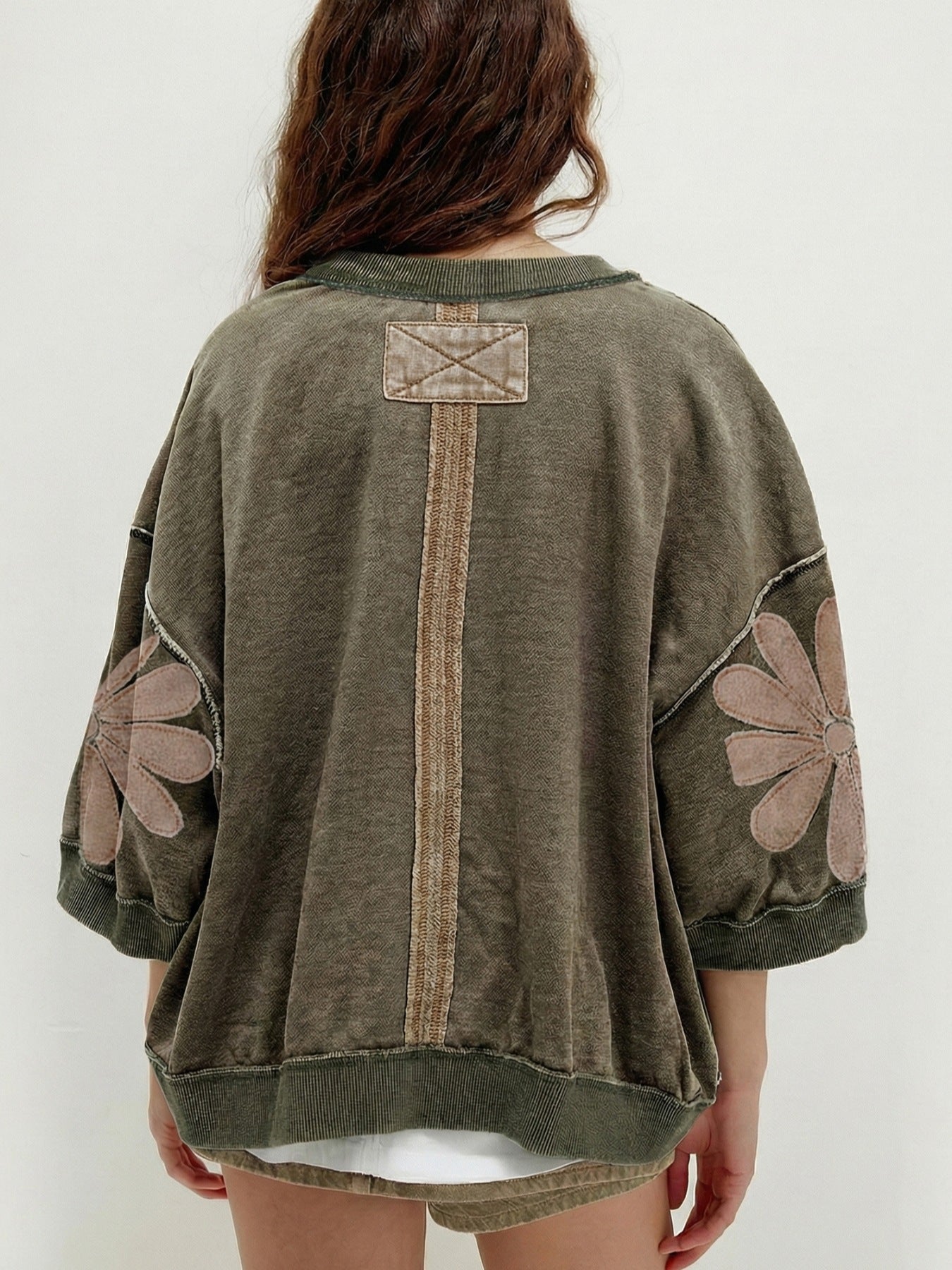 Relaxed pullover top with floral sleeve patch detail and exposed seams