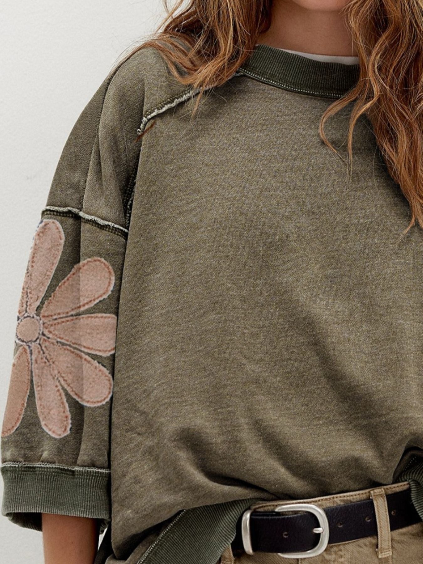 Relaxed pullover top with floral sleeve patch detail and exposed seams