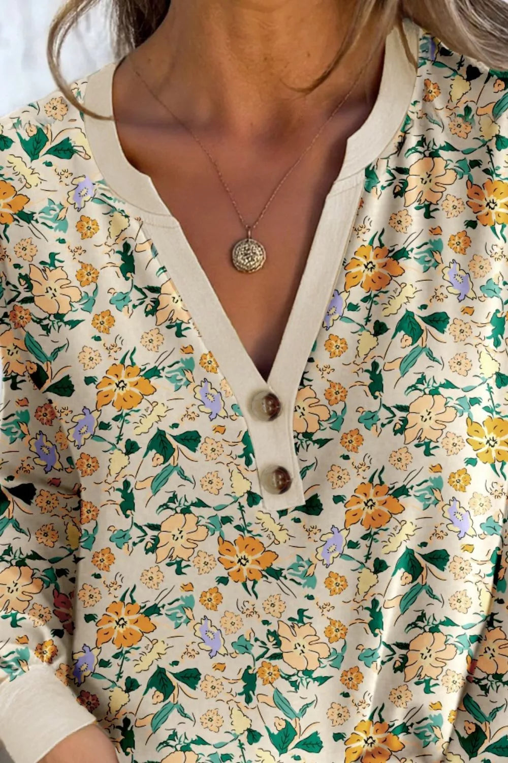 Cream floral long-sleeve blouse with a buttoned V-neckline and cuffed sleeves, paired with jeans.