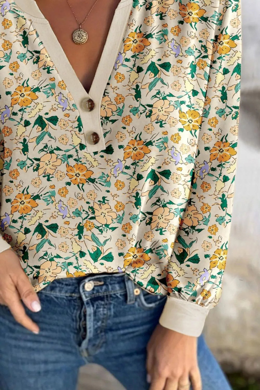 Cream floral long-sleeve blouse with a buttoned V-neckline and cuffed sleeves, paired with jeans.