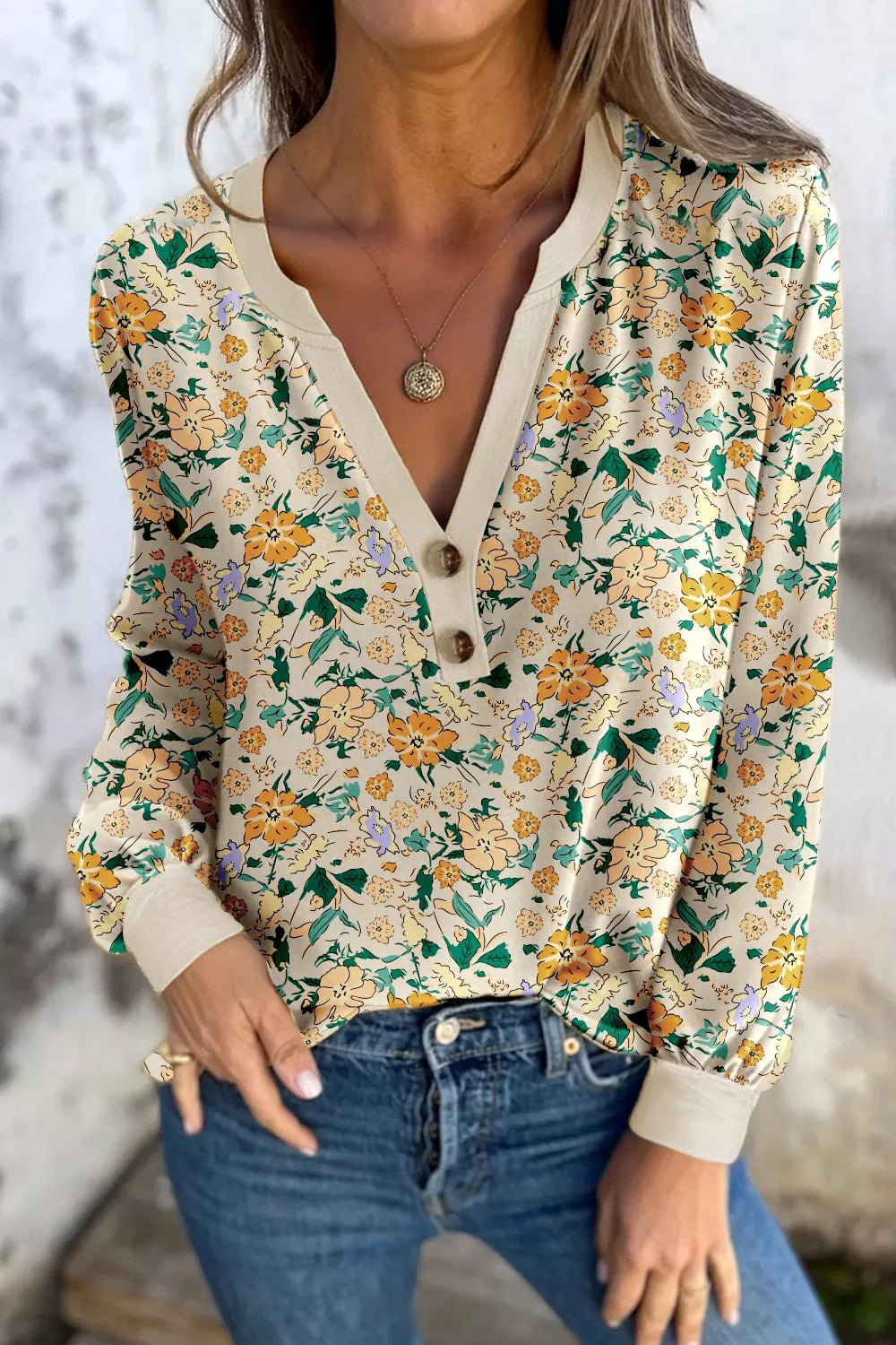 Cream floral long-sleeve blouse with a buttoned V-neckline and cuffed sleeves, paired with jeans.