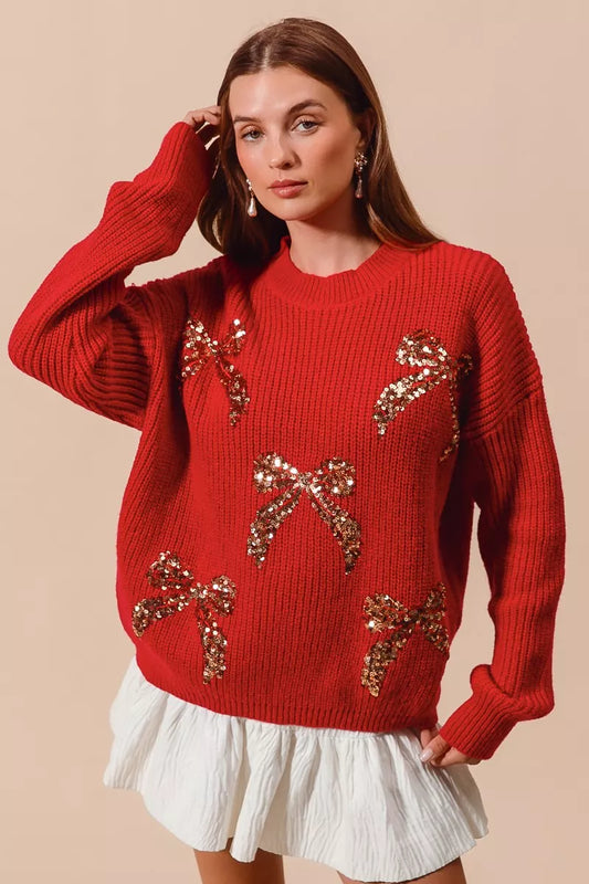 Woman wearing a red ribbed sweater with gold sequin bow designs — festive holiday sweater from A Whimsical Affair.