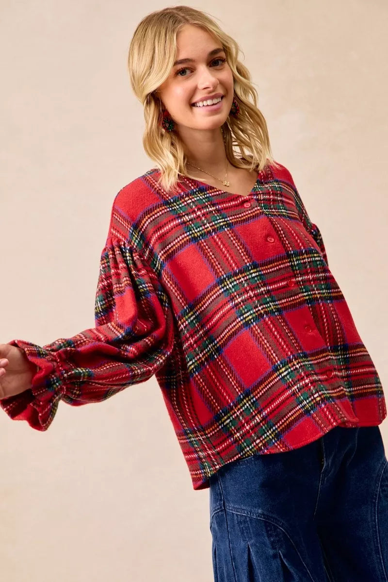 Woman wearing a festive red plaid button-front flounce-sleeve jacket with a v-neckline, styled for the holiday season.