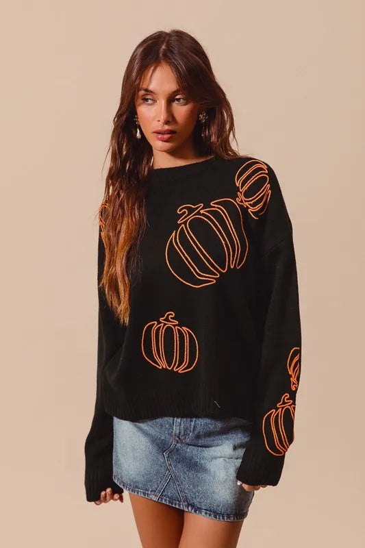 Woman wearing a black knit sweater with orange pumpkin outlines, styled with denim skirt — cozy Halloween pullover from A Whimsical Affair.