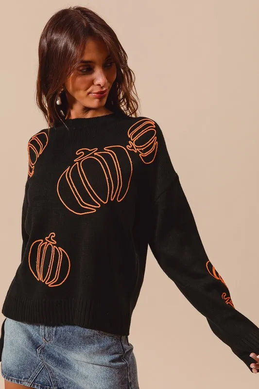 Woman wearing a black knit sweater with orange pumpkin outlines, styled with denim skirt — cozy Halloween pullover from A Whimsical Affair.