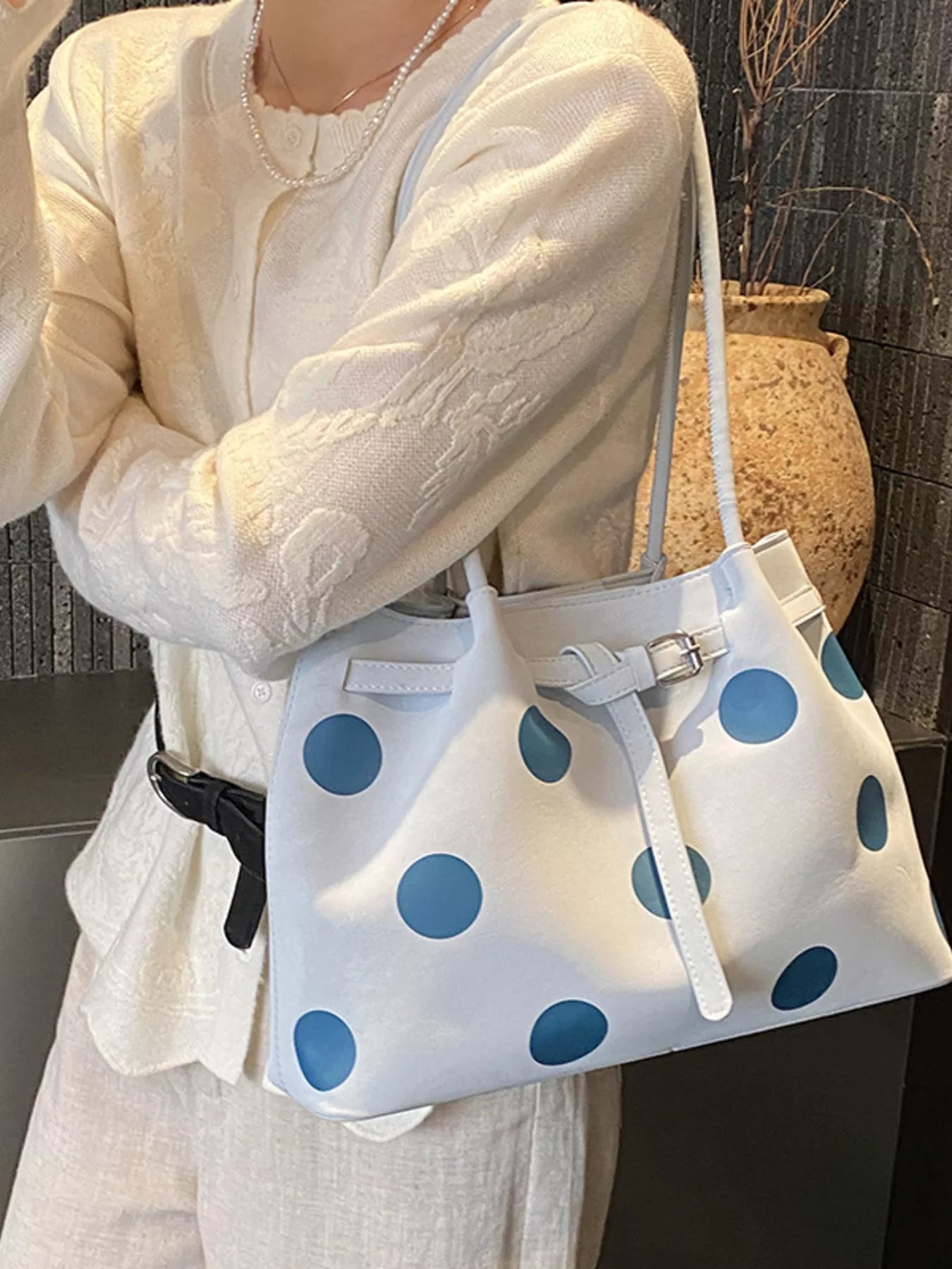 Medium white slouch shoulder bag with bold blue polka dots, PU leather material, adjustable strap detail, and relaxed everyday styling.