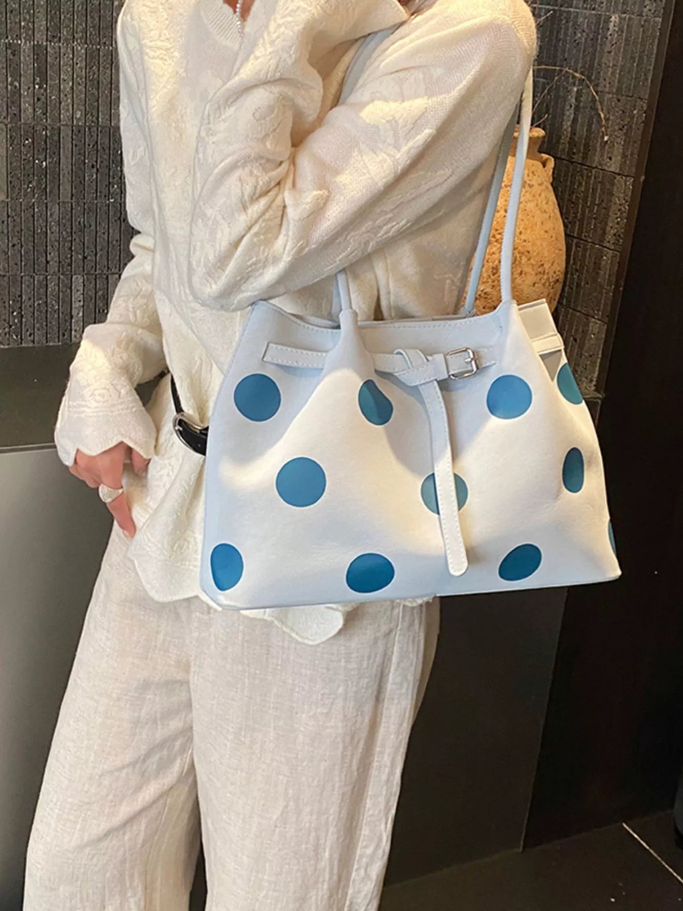 Medium white slouch shoulder bag with bold blue polka dots, PU leather material, adjustable strap detail, and relaxed everyday styling.