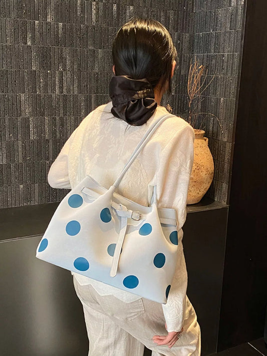 Medium white slouch shoulder bag with bold blue polka dots, PU leather material, adjustable strap detail, and relaxed everyday styling.