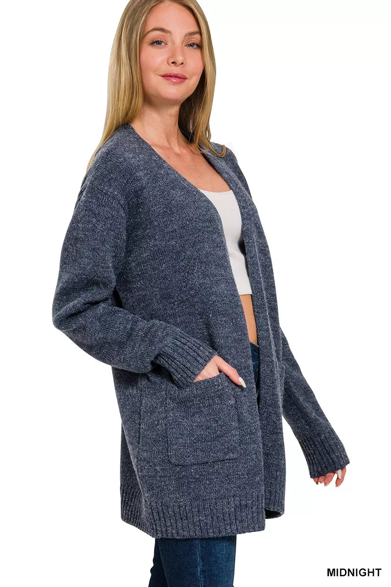 Open-front knit cardigan with front pockets, ribbed trim, long sleeves, and a relaxed slightly stretchy fit styled with jeans.