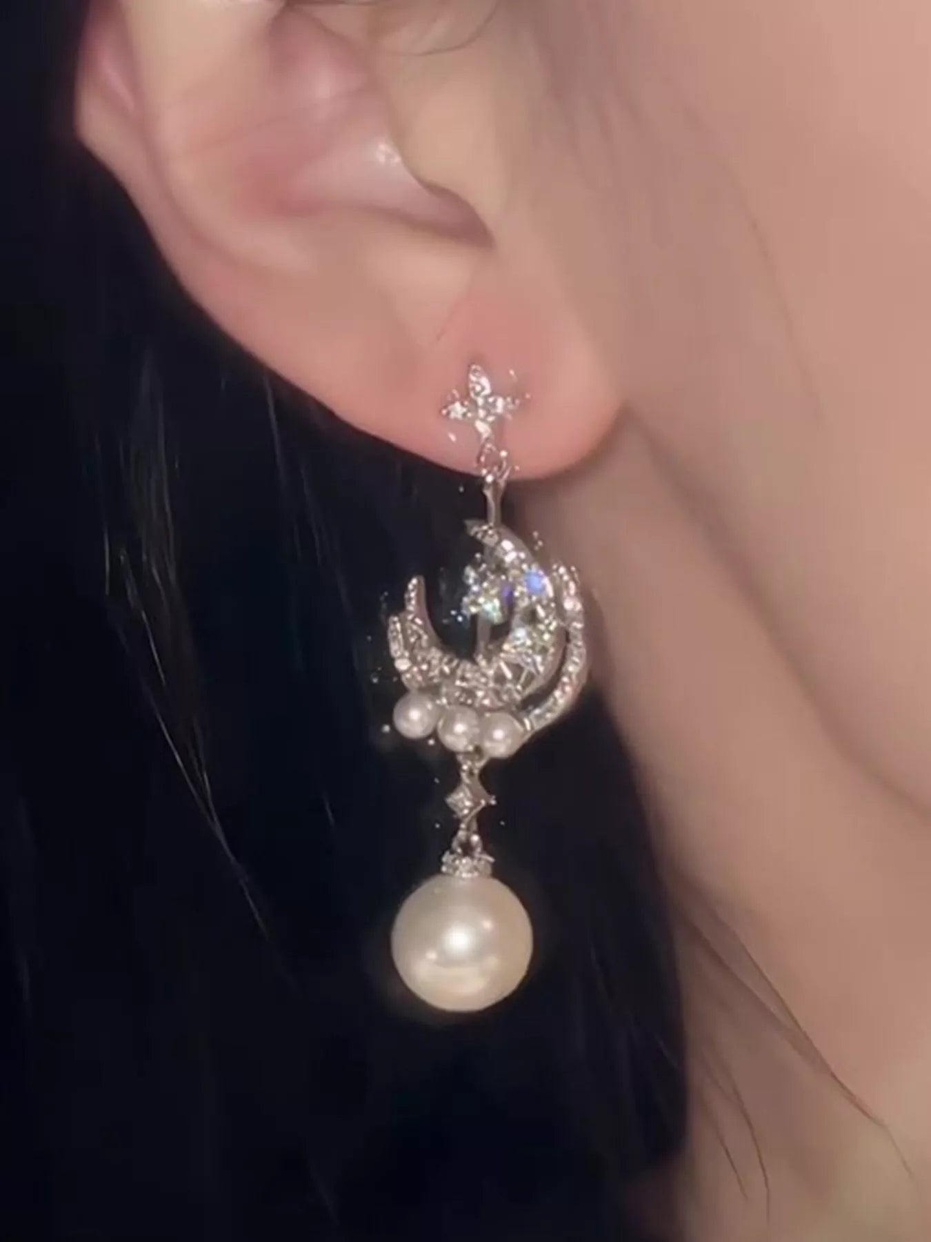 Silver celestial dangle earrings with crescent moon charms, zircon star accents, and synthetic pearl drops worn on the ear.