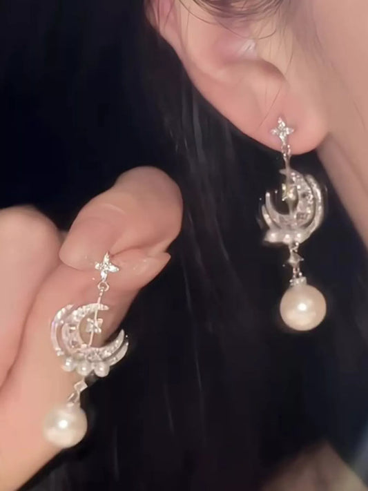 Silver celestial dangle earrings with crescent moon charms, zircon star accents, and synthetic pearl drops worn on the ear.