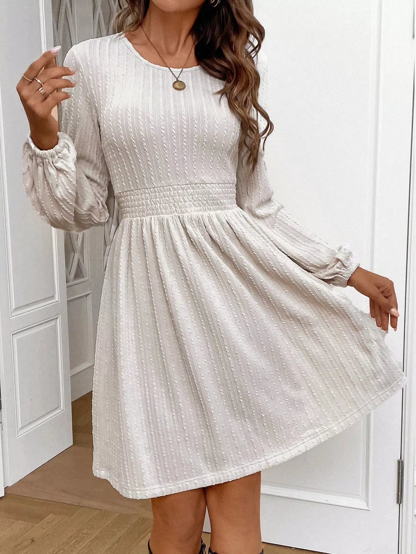 Cream long-sleeve textured mini dress with smocked waist worn indoors.