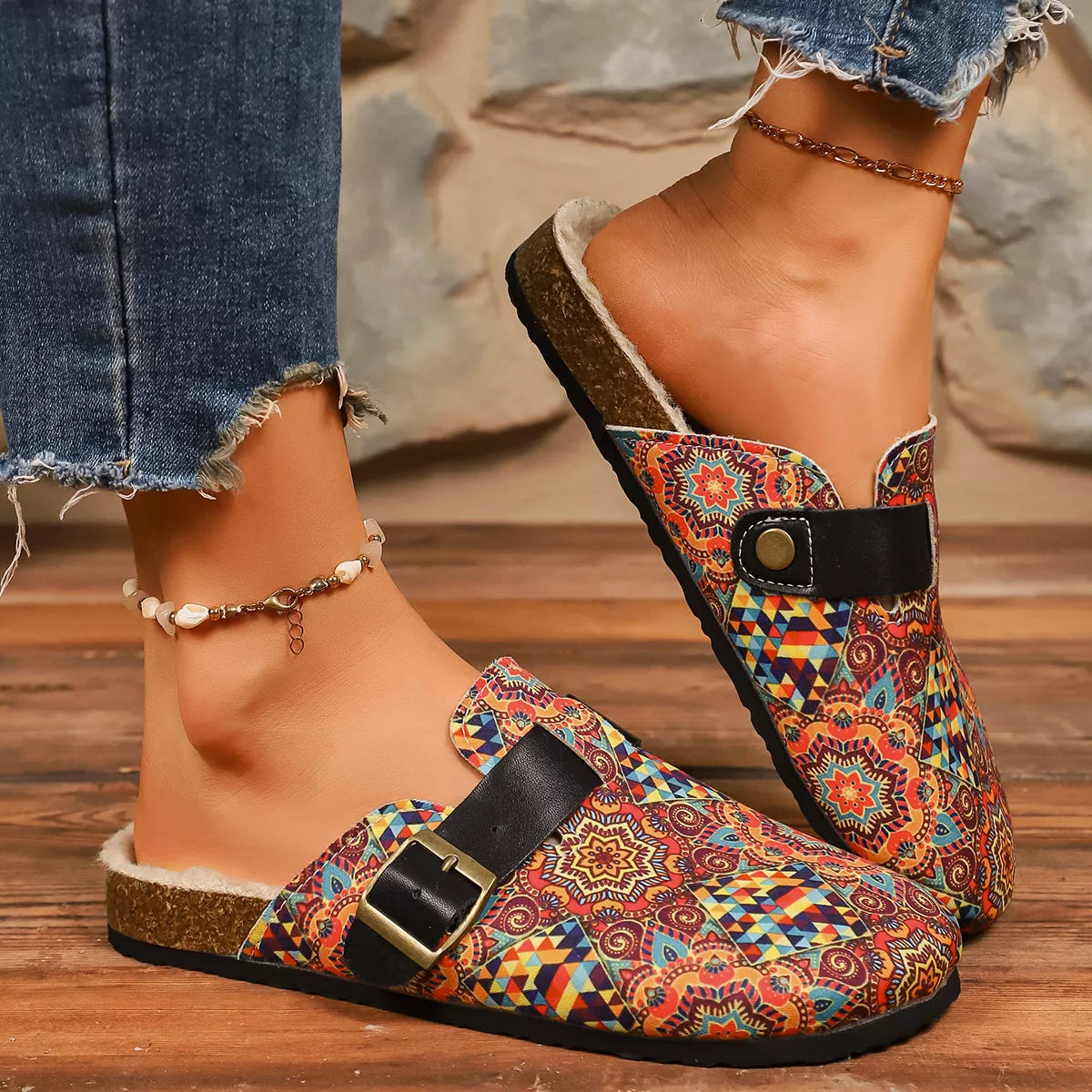 Colorful geometric patterned clogs with black buckle strap and flat sole, styled with ankle bracelets.