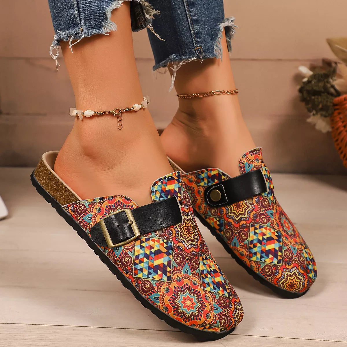 Colorful geometric patterned clogs with black buckle strap and flat sole, styled with ankle bracelets.