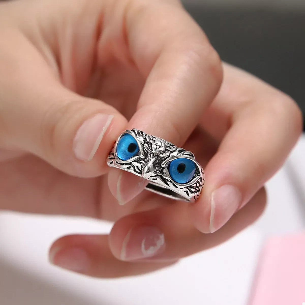 A silver-plated alloy ring with detailed owl features and vivid blue resin eyes, called the Nocturne Gaze Ring.