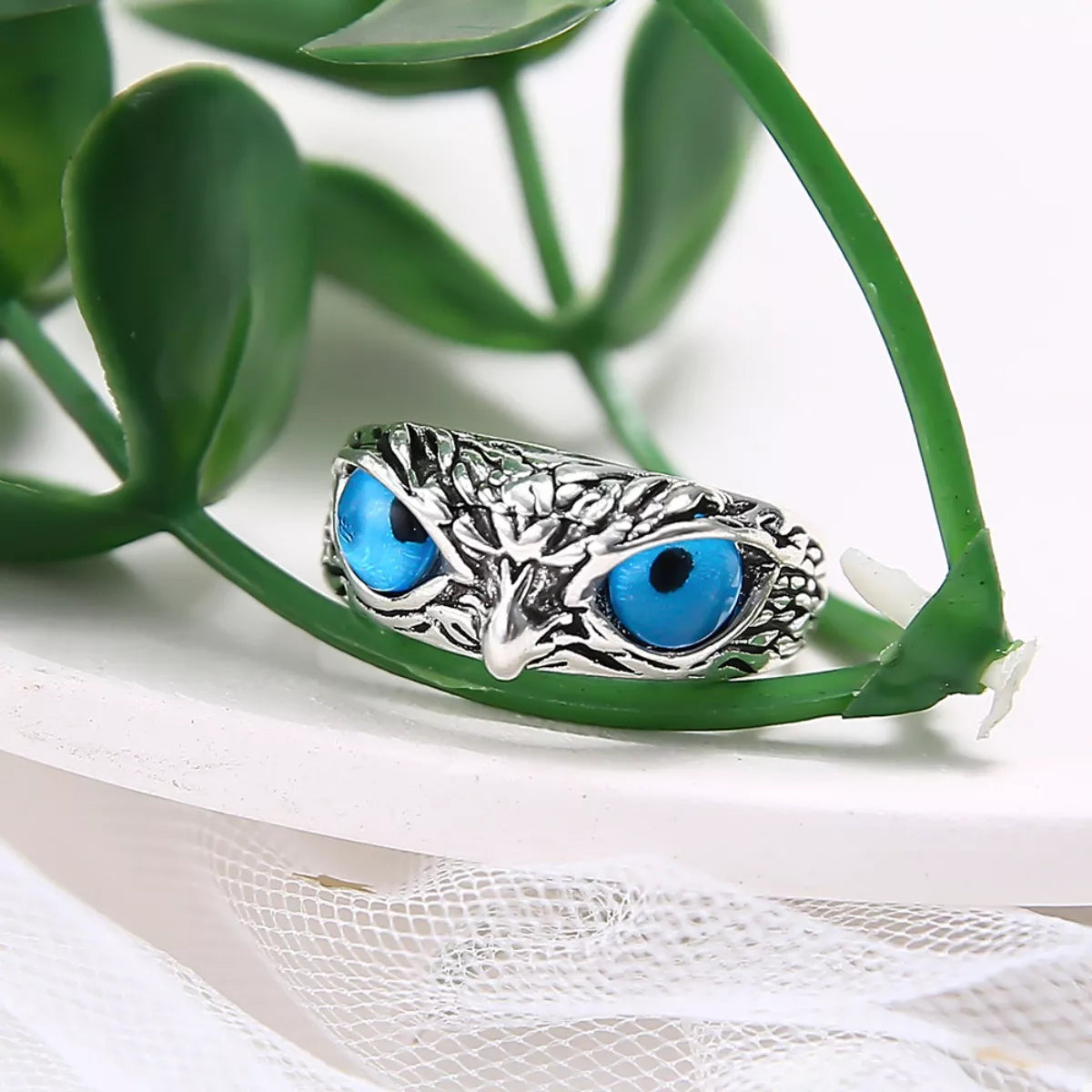A silver-plated alloy ring with detailed owl features and vivid blue resin eyes, called the Nocturne Gaze Ring.