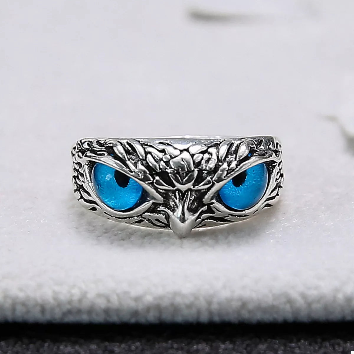 A silver-plated alloy ring with detailed owl features and vivid blue resin eyes, called the Nocturne Gaze Ring.