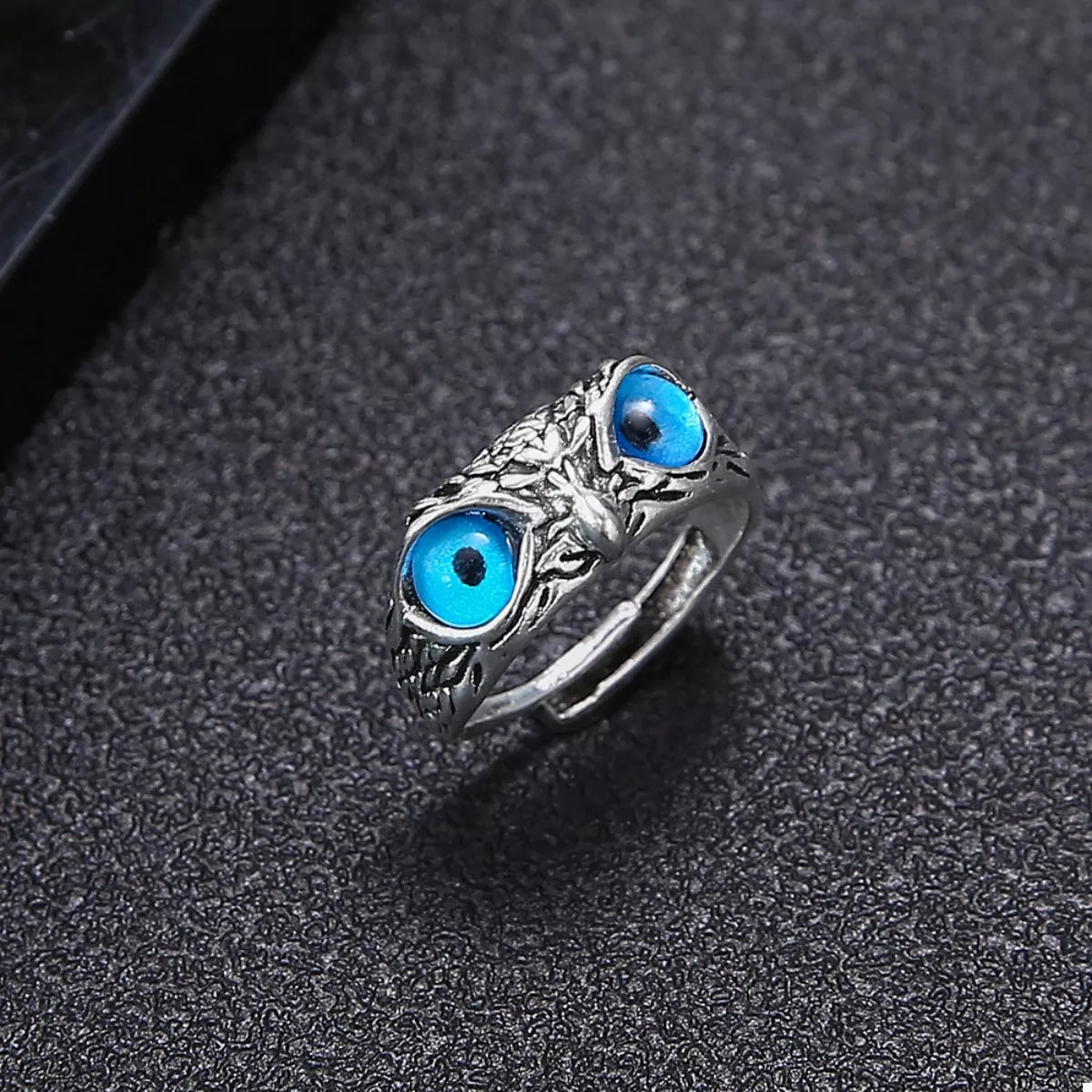 A silver-plated alloy ring with detailed owl features and vivid blue resin eyes, called the Nocturne Gaze Ring.