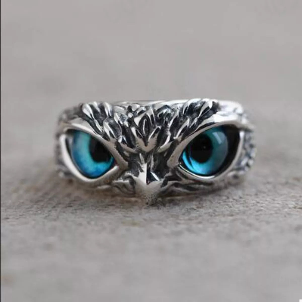 A silver-plated alloy ring with detailed owl features and vivid blue resin eyes, called the Nocturne Gaze Ring.