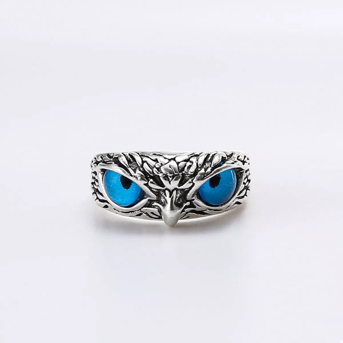 A silver-plated alloy ring with detailed owl features and vivid blue resin eyes, called the Nocturne Gaze Ring.