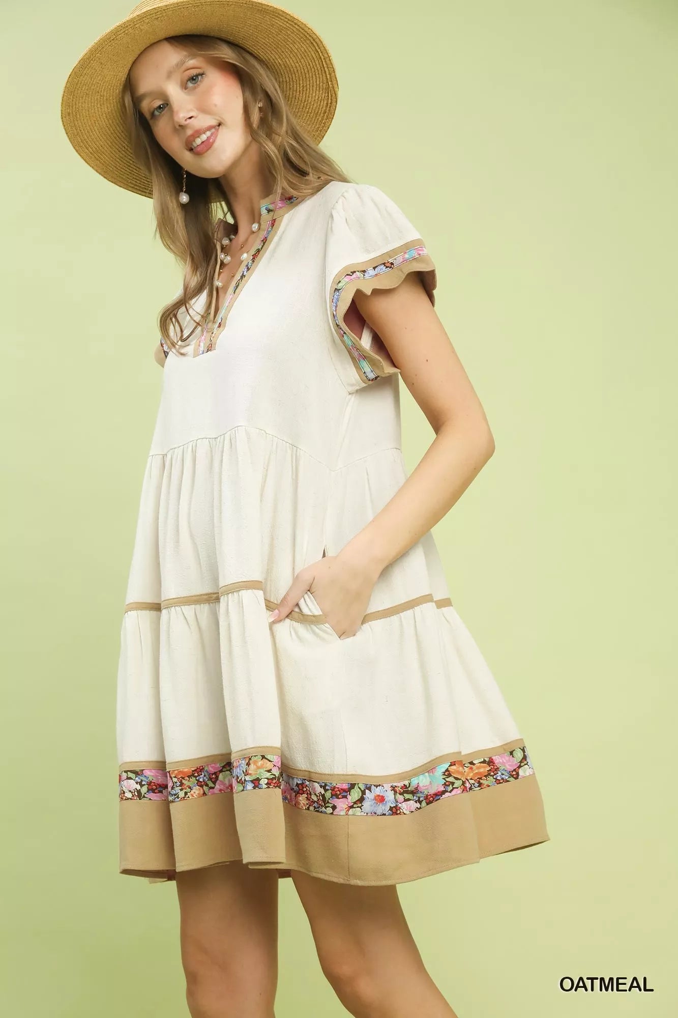 Oatmeal linen tiered mini dress with flutter sleeves, split V-neck, and colorful floral trim detailing.