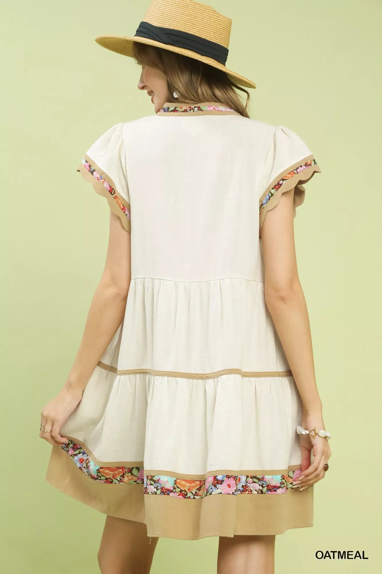 Oatmeal linen tiered mini dress with flutter sleeves, split V-neck, and colorful floral trim detailing.