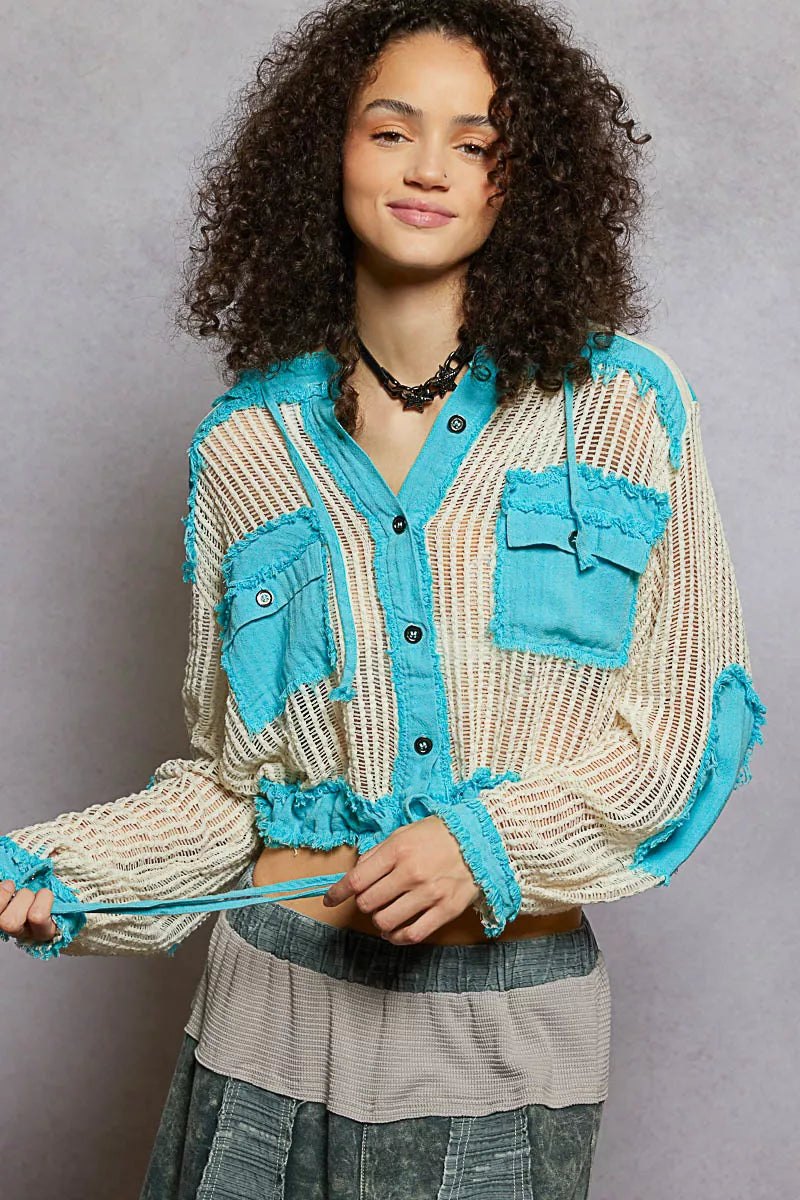Model wearing an ivory woven hooded button-down top with turquoise contrast patches, cropped drawstring hem, and front pockets.