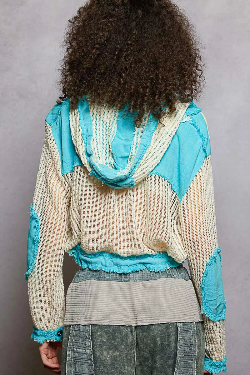 Model wearing an ivory woven hooded button-down top with turquoise contrast patches, cropped drawstring hem, and front pockets.