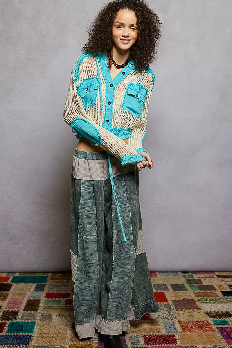 Model wearing an ivory woven hooded button-down top with turquoise contrast patches, cropped drawstring hem, and front pockets.