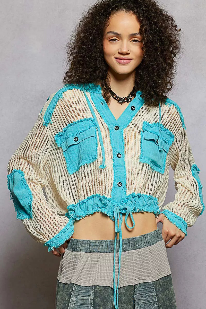 Model wearing an ivory woven hooded button-down top with turquoise contrast patches, cropped drawstring hem, and front pockets.