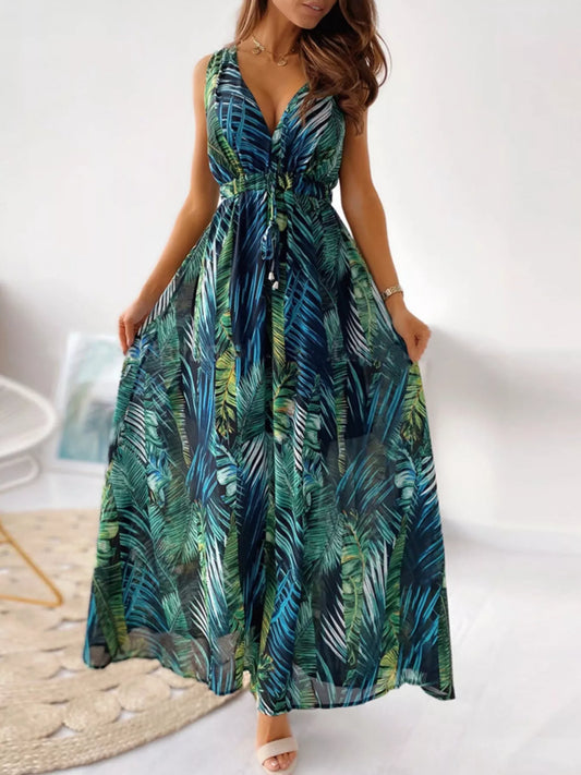 A flowy sleeveless maxi dress with a deep V-neckline and green/blue palm leaf print, styled with a drawstring waist.