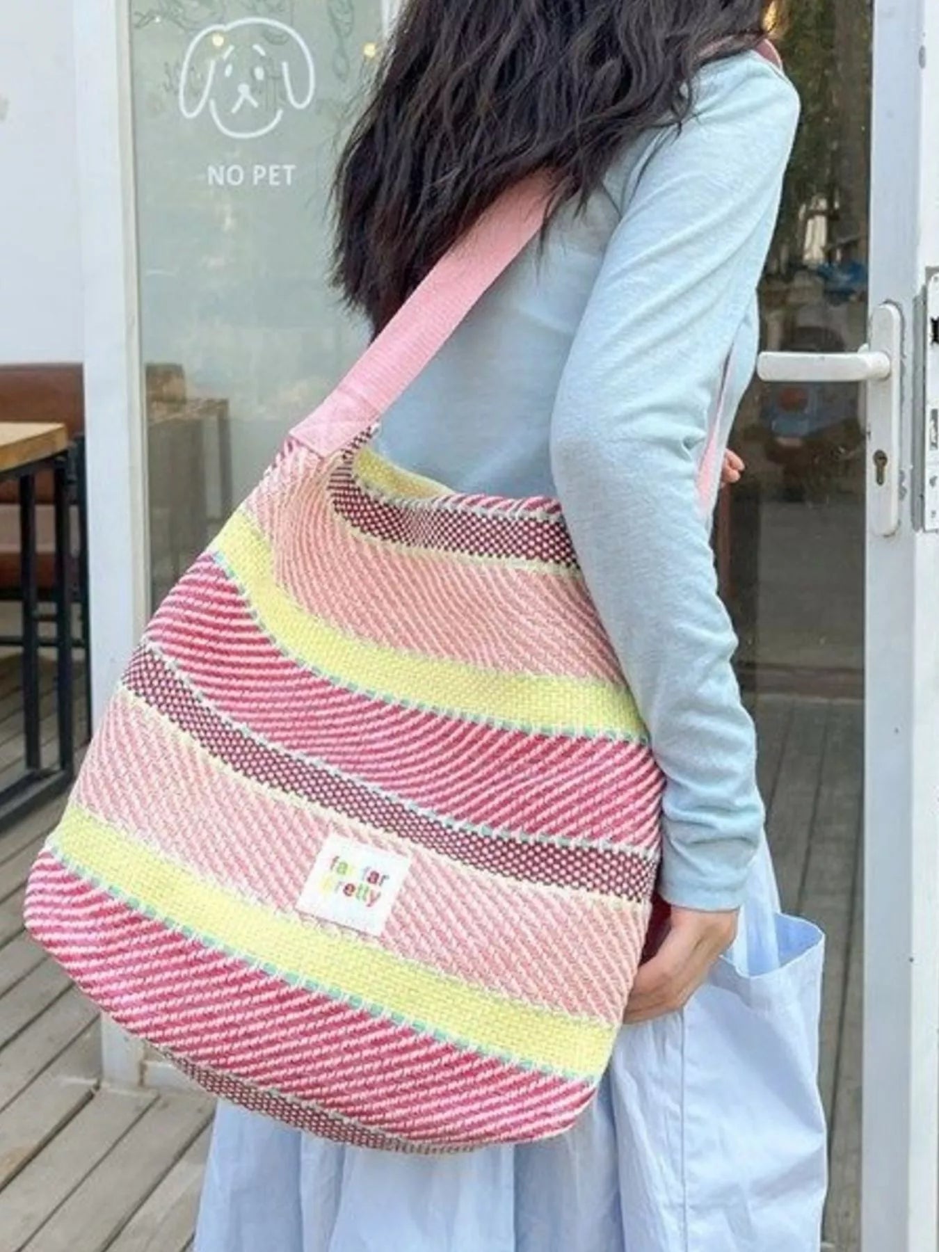 Large pastel striped woven tote bag with shoulder strap worn casually outdoors