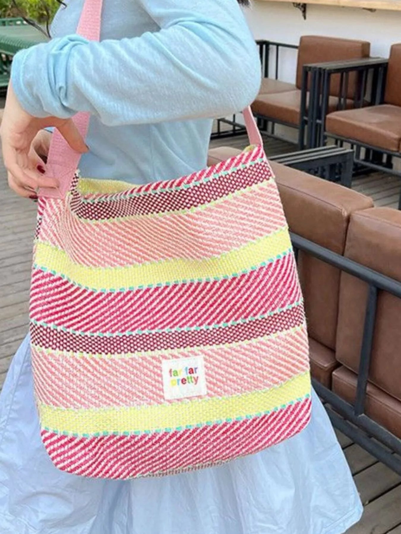 Large pastel striped woven tote bag with shoulder strap worn casually outdoors