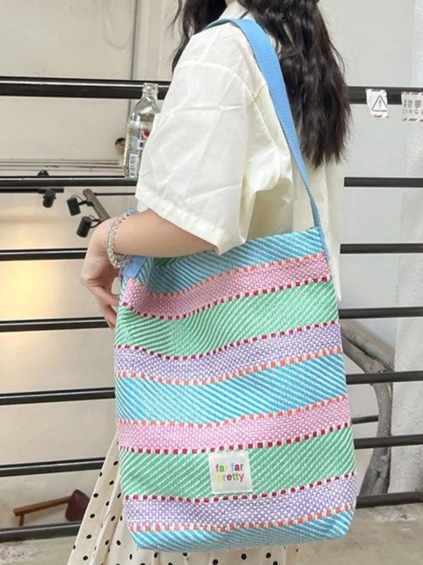 Large pastel striped woven tote bag with shoulder strap worn casually outdoors