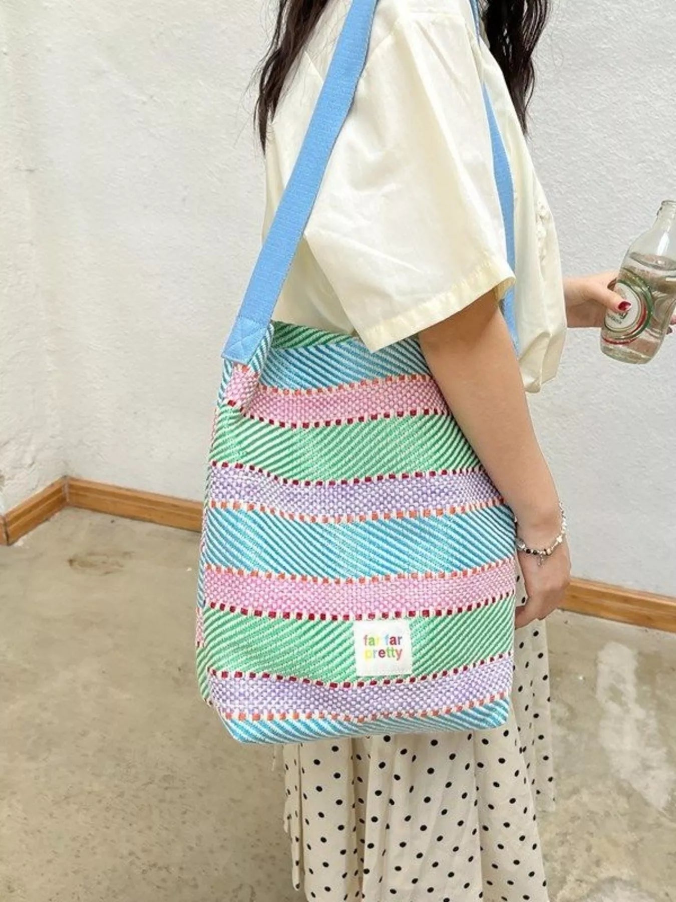 Large pastel striped woven tote bag with shoulder strap worn casually outdoors