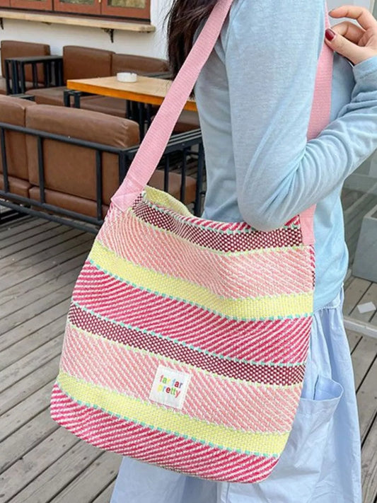 Large pastel striped woven tote bag with shoulder strap worn casually outdoors