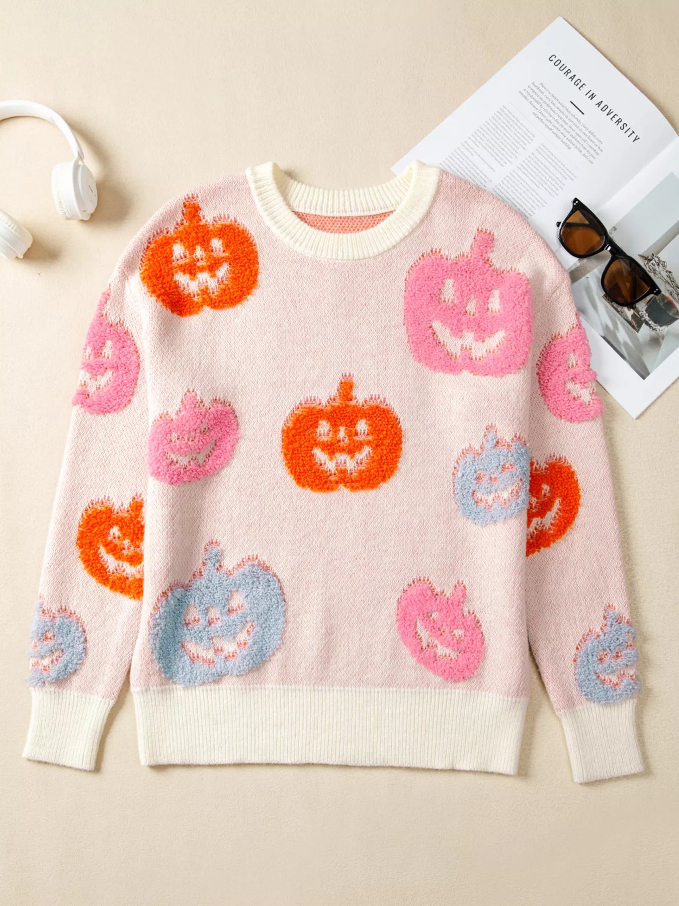 Woman wearing a cream sweater decorated with pastel orange, pink, and blue textured jack-o’-lanterns — cozy Halloween sweater from A Whimsical Affair.
