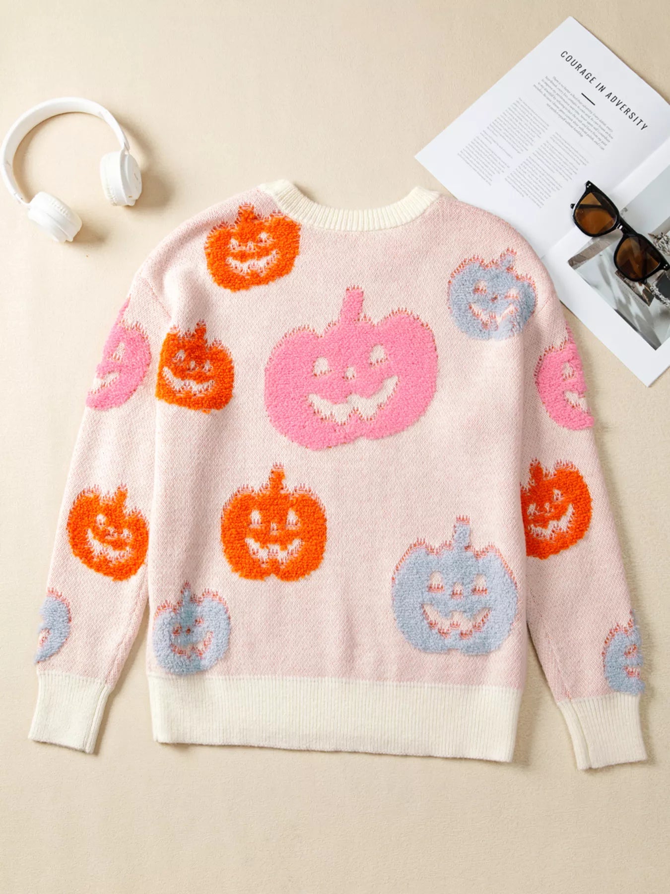 Woman wearing a cream sweater decorated with pastel orange, pink, and blue textured jack-o’-lanterns — cozy Halloween sweater from A Whimsical Affair.