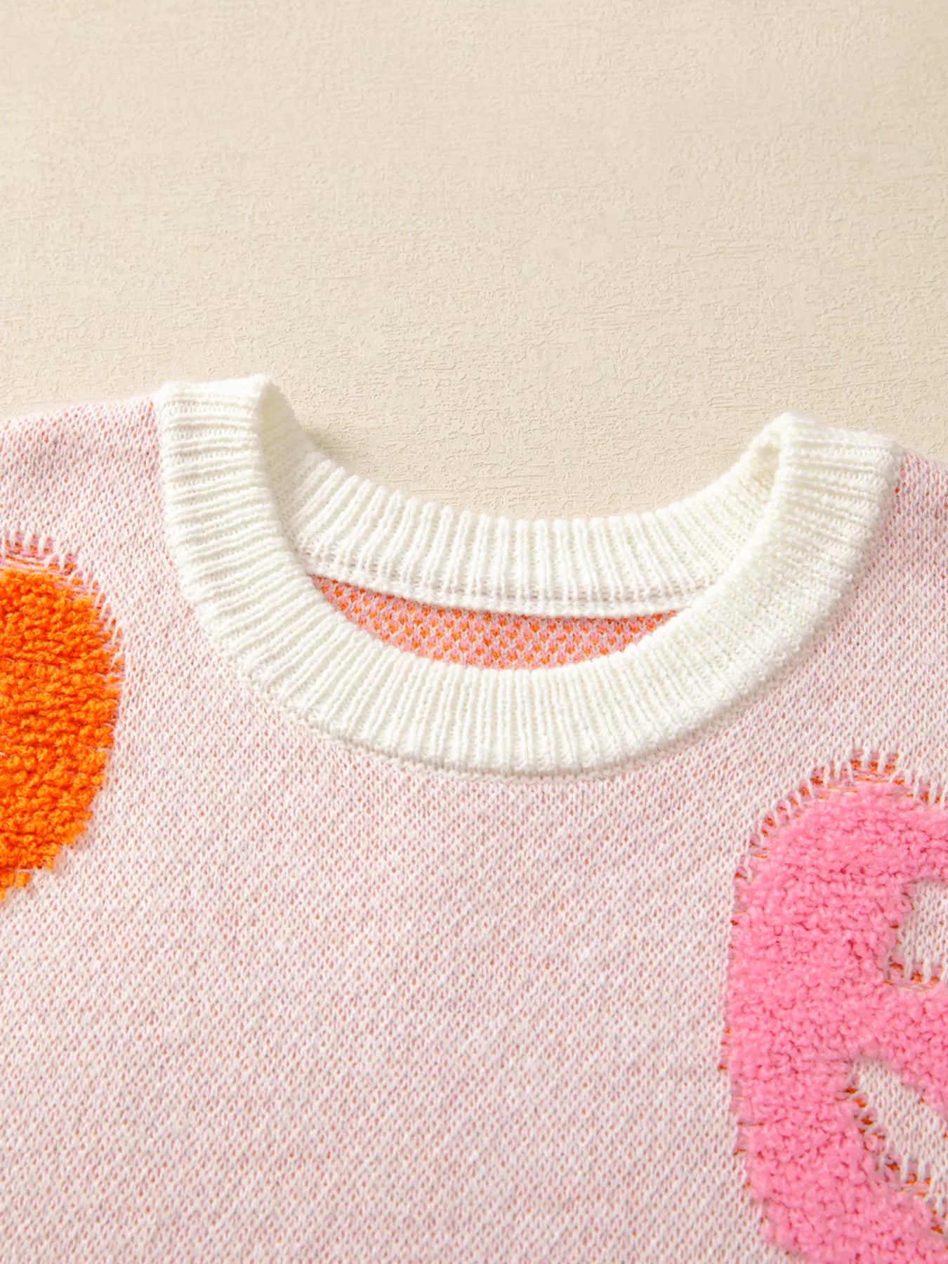 Woman wearing a cream sweater decorated with pastel orange, pink, and blue textured jack-o’-lanterns — cozy Halloween sweater from A Whimsical Affair.