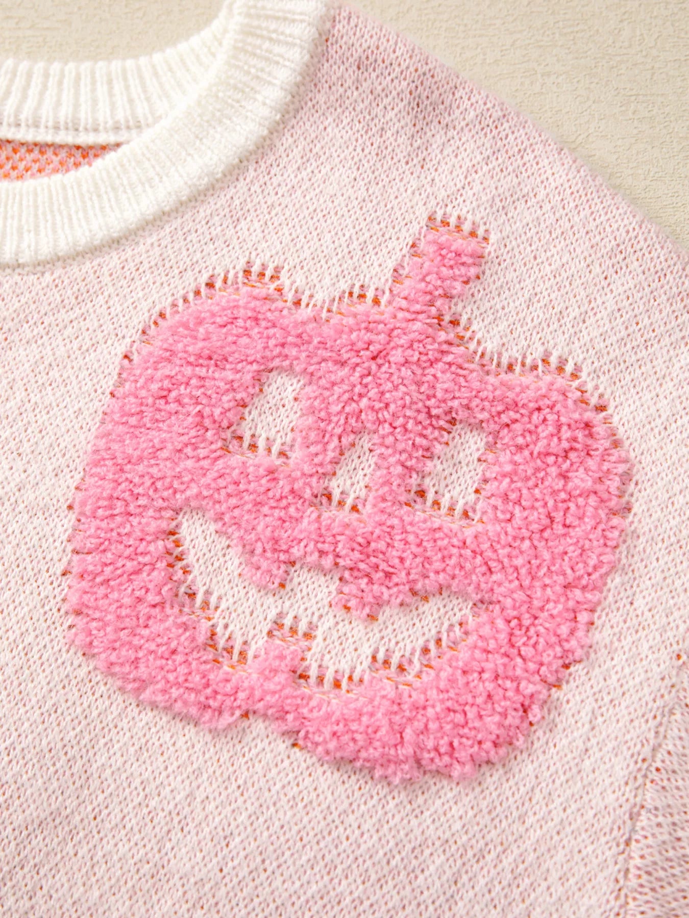 Woman wearing a cream sweater decorated with pastel orange, pink, and blue textured jack-o’-lanterns — cozy Halloween sweater from A Whimsical Affair.