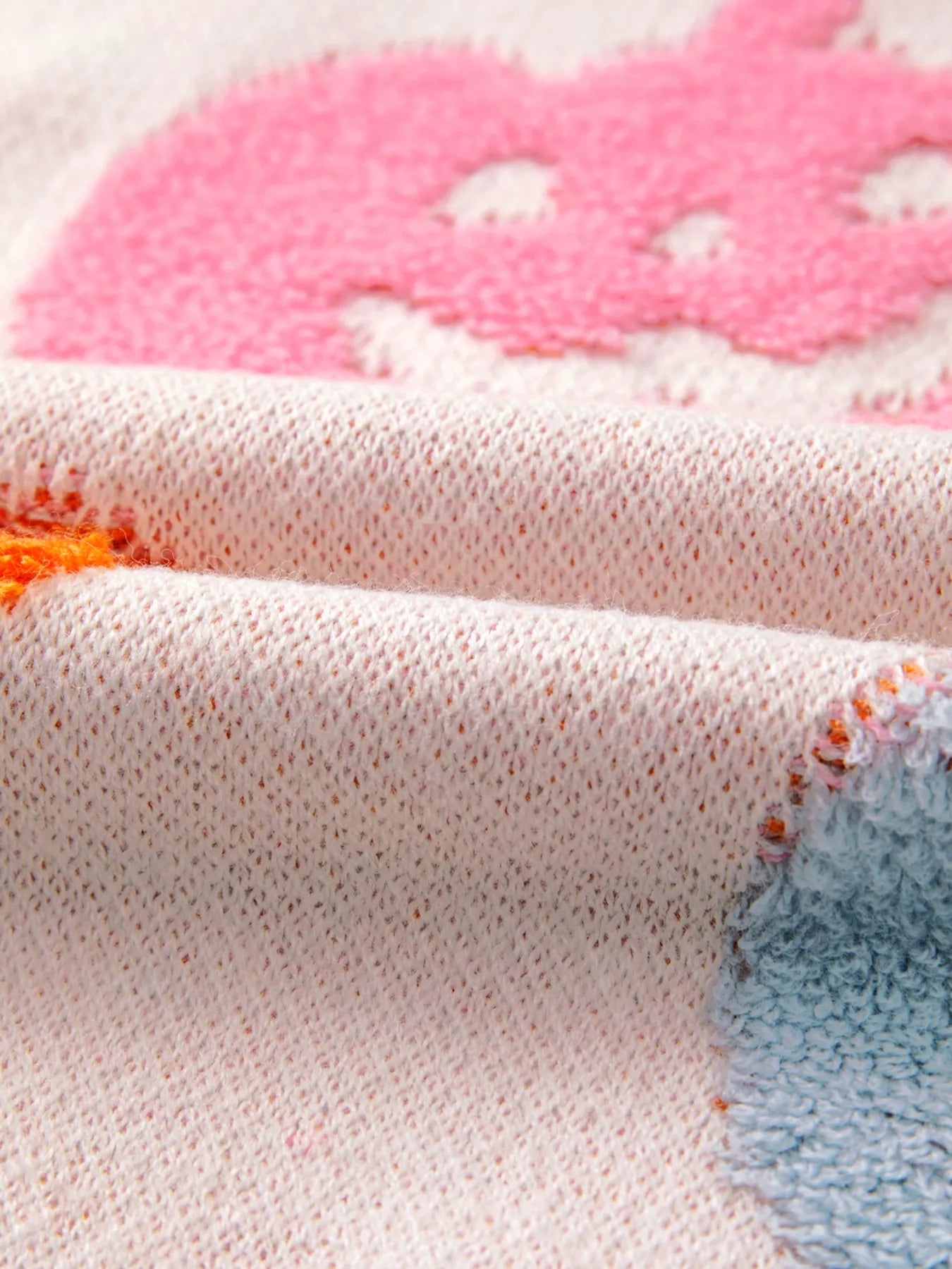Woman wearing a cream sweater decorated with pastel orange, pink, and blue textured jack-o’-lanterns — cozy Halloween sweater from A Whimsical Affair.