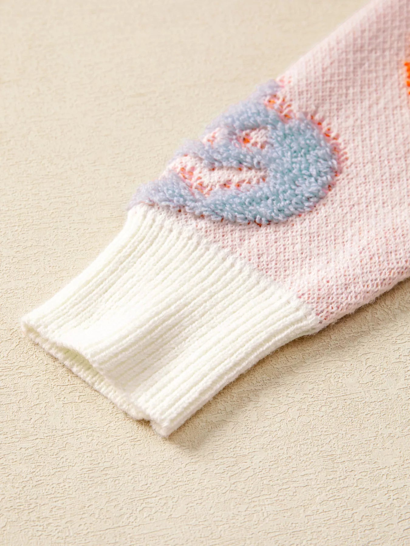 Woman wearing a cream sweater decorated with pastel orange, pink, and blue textured jack-o’-lanterns — cozy Halloween sweater from A Whimsical Affair.