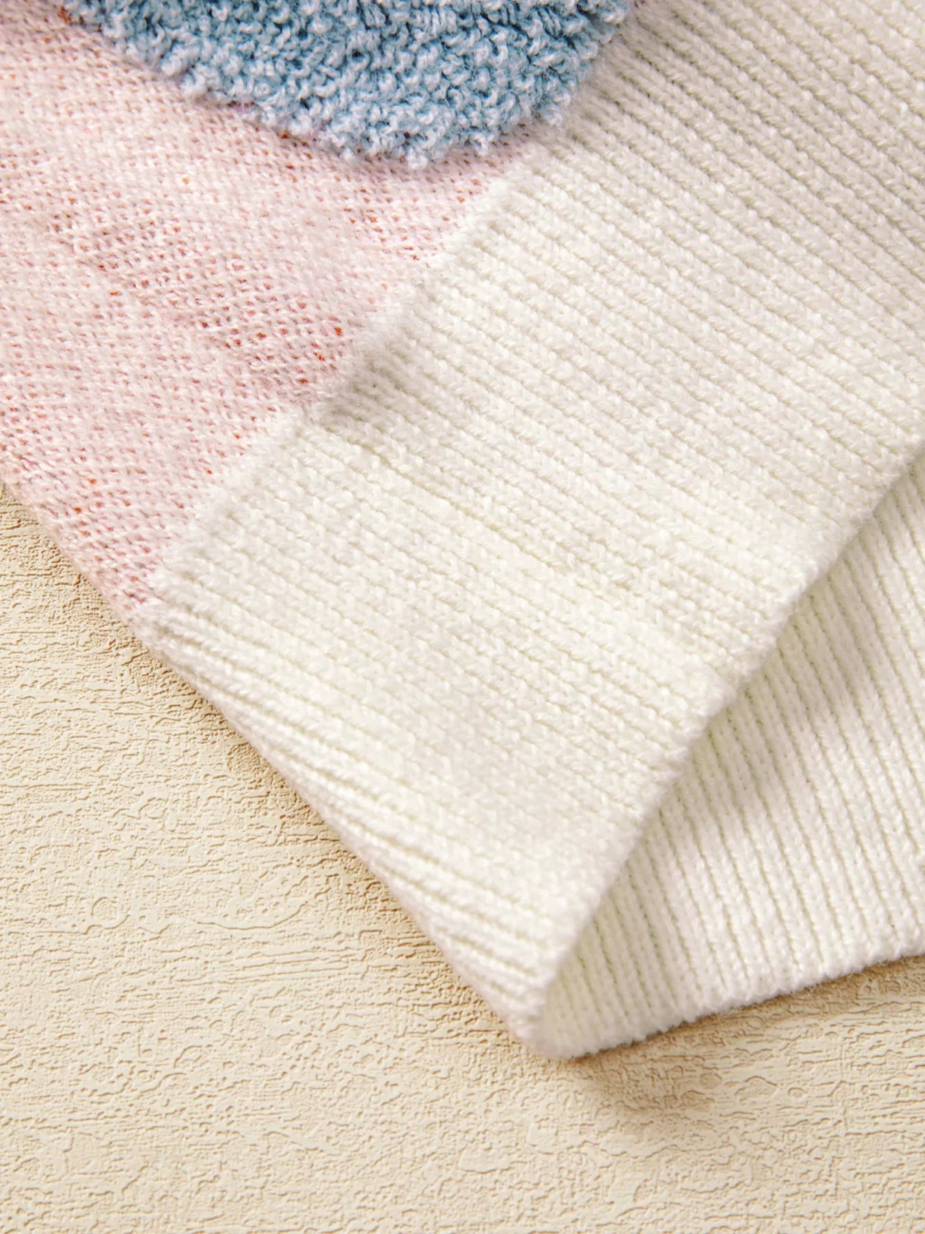 Woman wearing a cream sweater decorated with pastel orange, pink, and blue textured jack-o’-lanterns — cozy Halloween sweater from A Whimsical Affair.