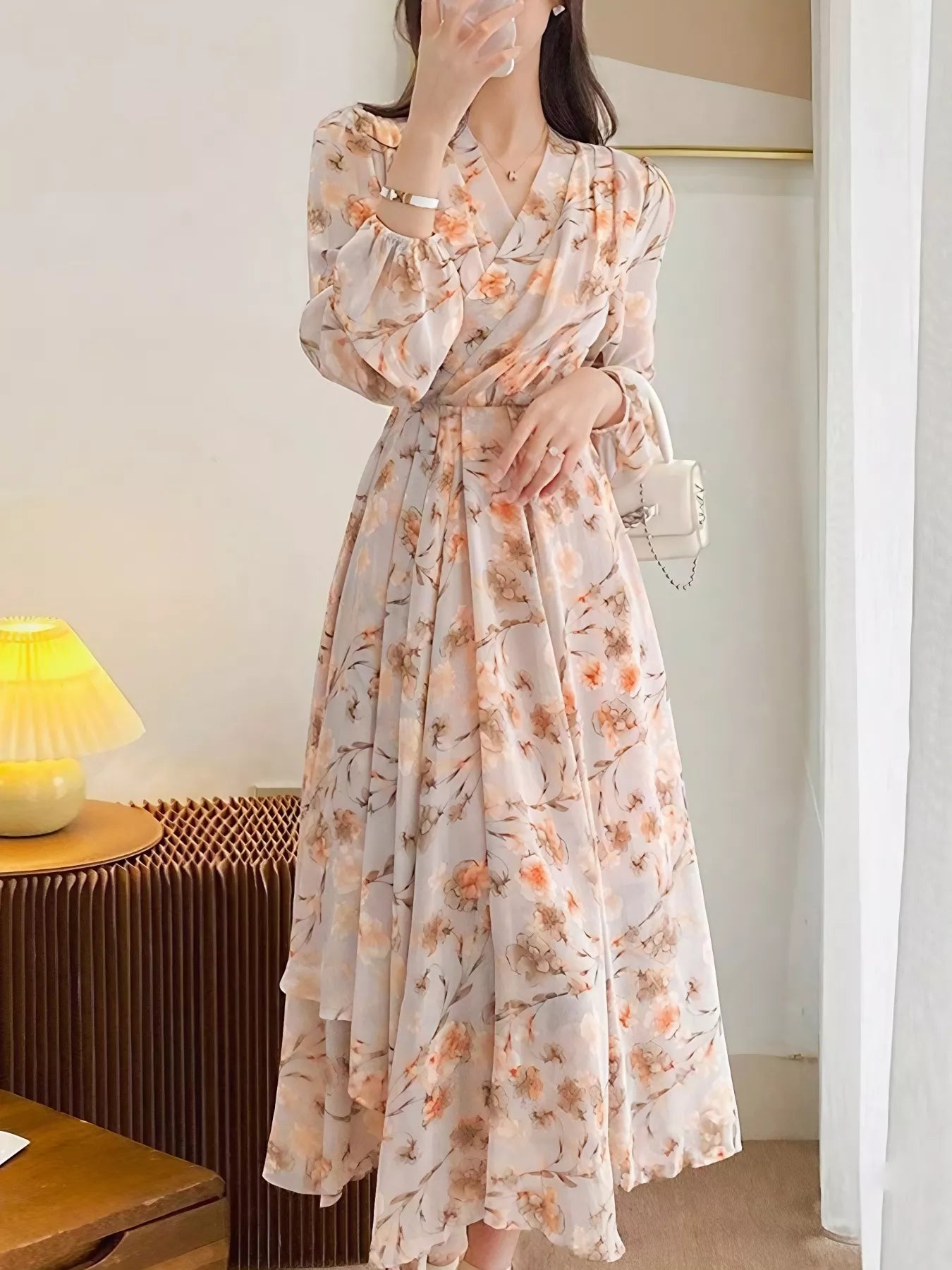 Model wearing the Peach Blossom Chiffon Midi Dress with long puff sleeves and peach floral print, styled with a white shoulder bag.