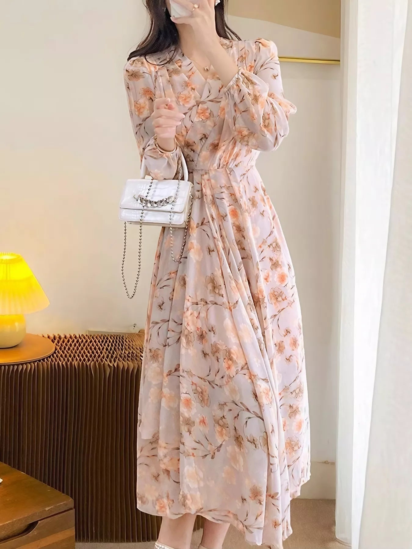 Model wearing the Peach Blossom Chiffon Midi Dress with long puff sleeves and peach floral print, styled with a white shoulder bag.