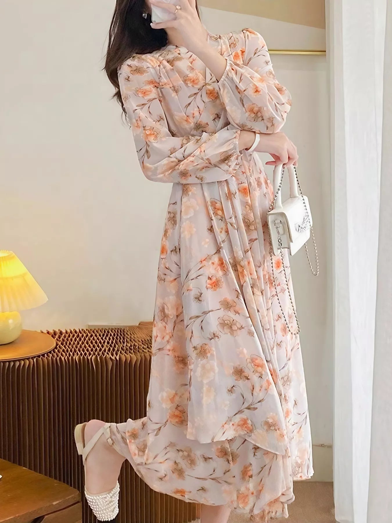 Model wearing the Peach Blossom Chiffon Midi Dress with long puff sleeves and peach floral print, styled with a white shoulder bag.