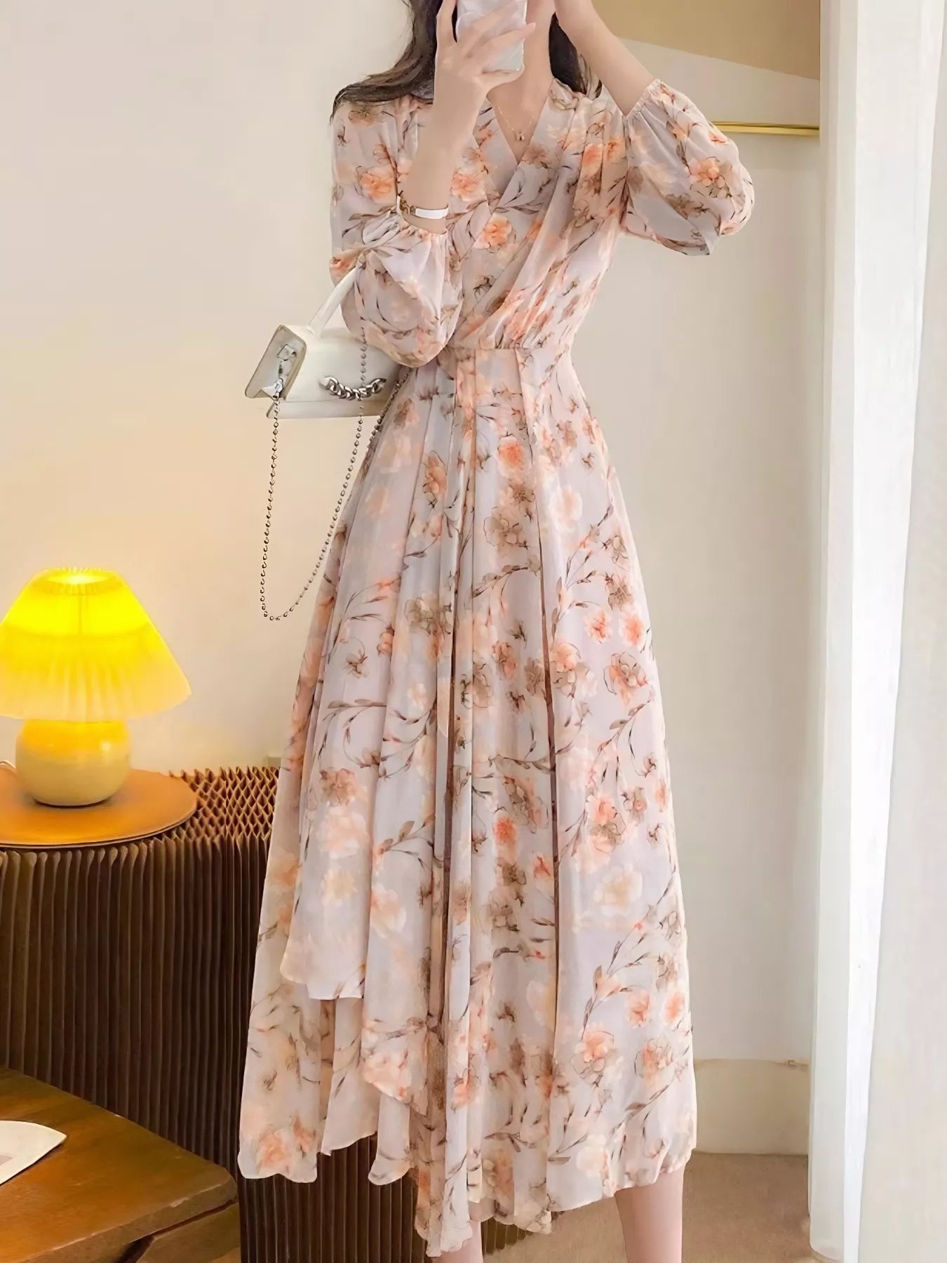 Model wearing the Peach Blossom Chiffon Midi Dress with long puff sleeves and peach floral print, styled with a white shoulder bag.