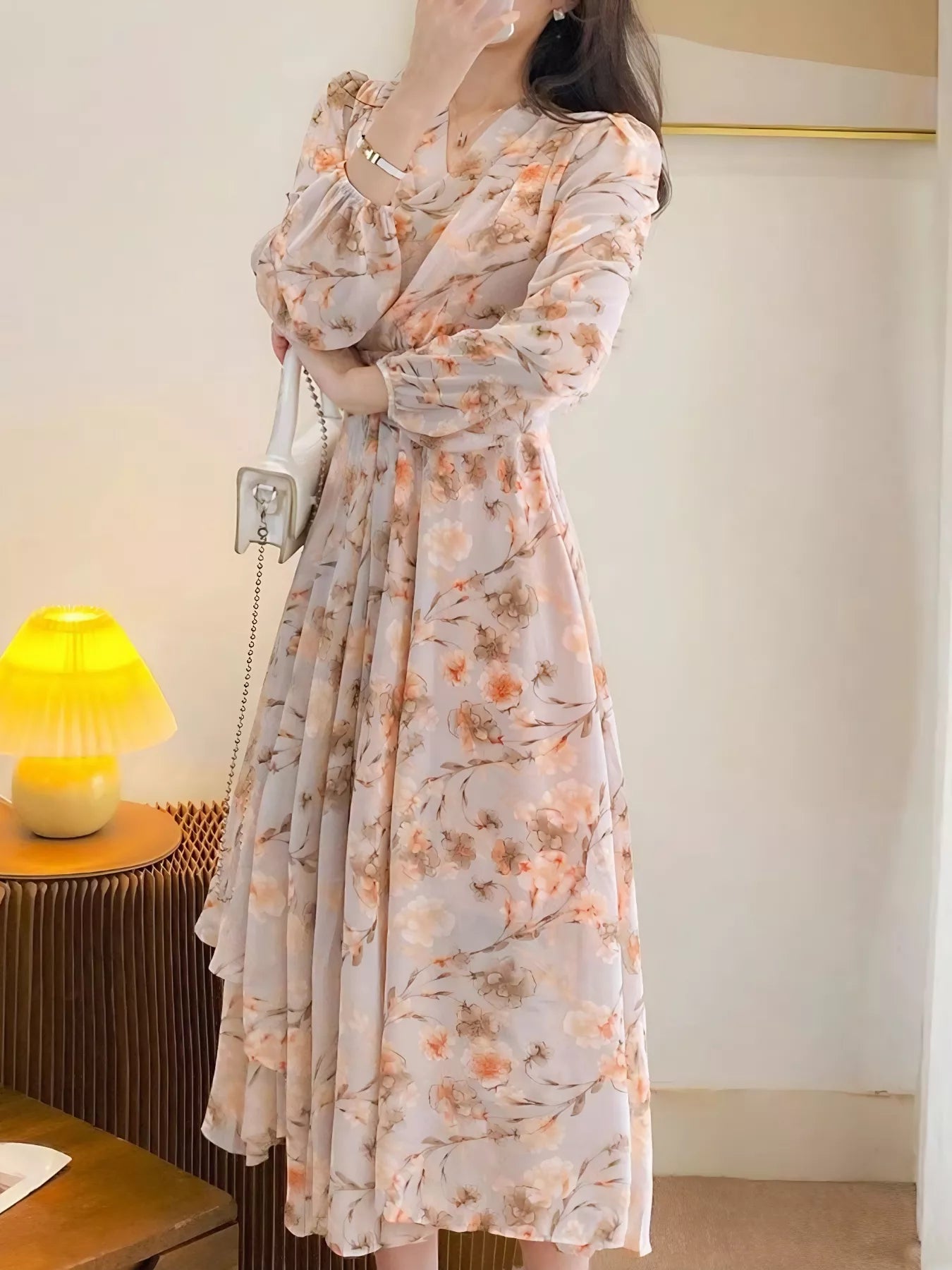 Model wearing the Peach Blossom Chiffon Midi Dress with long puff sleeves and peach floral print, styled with a white shoulder bag.