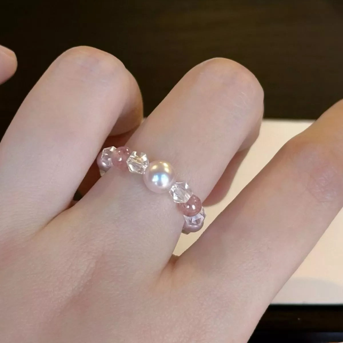 Dainty ring with a synthetic pearl accent and crystal bead details worn on a finger.